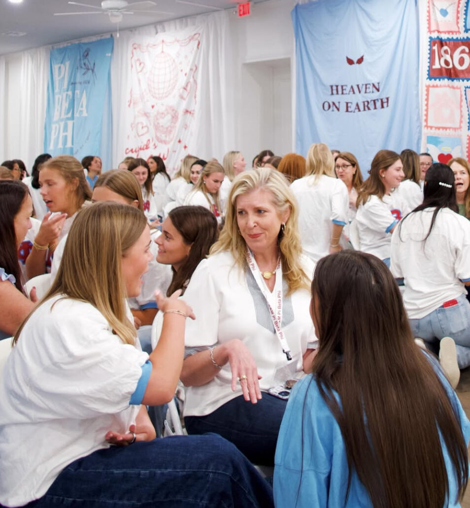 A group of members wearing white t-shirts inside speaking with one another with white and blue banners in the background