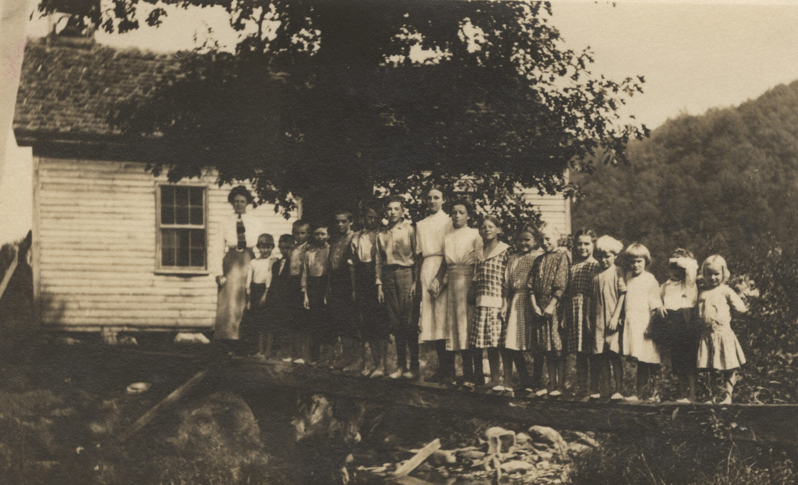 Several children and a teacher standing outside a school house