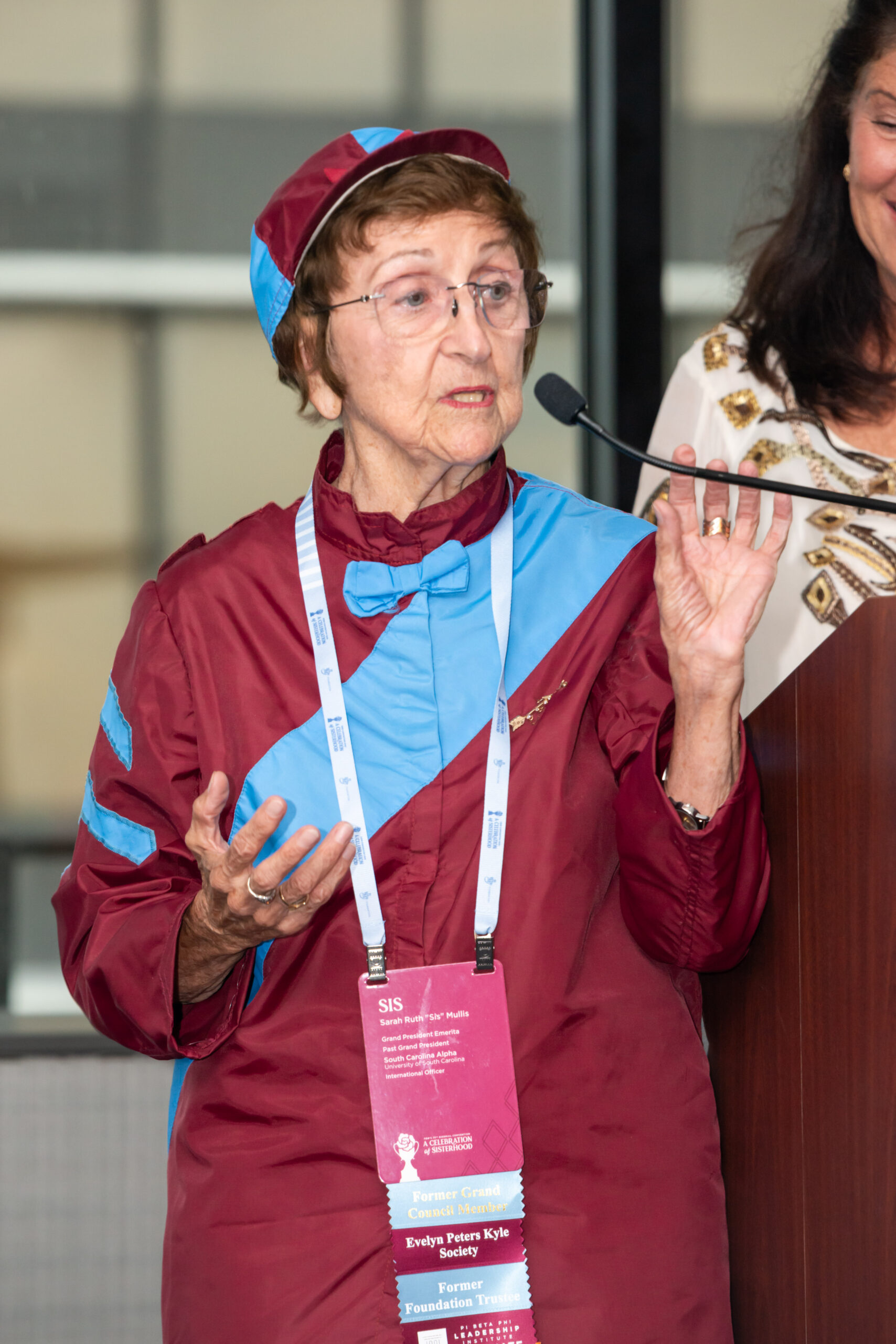 Member wearing wine and silver blue racing top and hat while speaking into a microphone