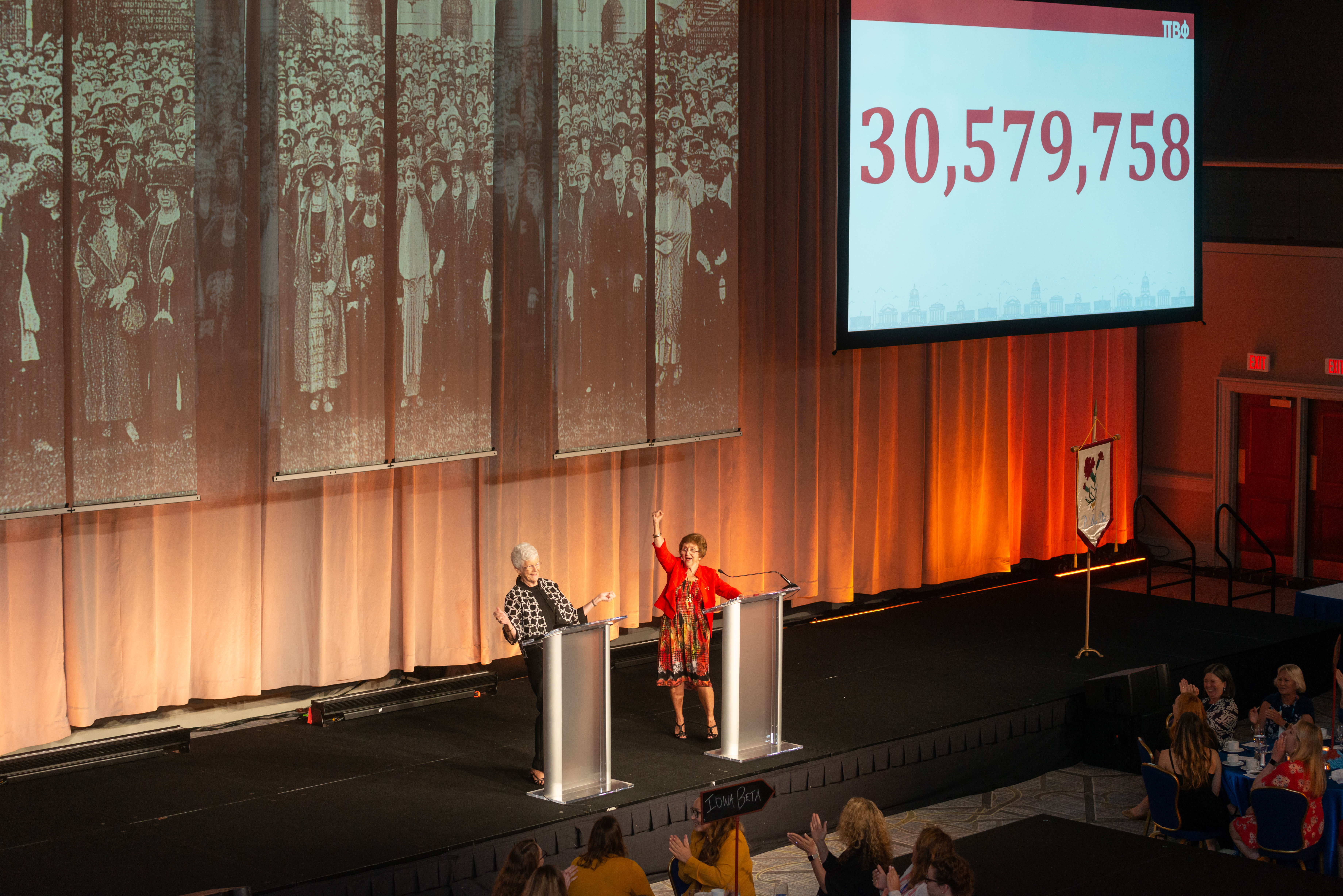 Two members standing behind podiums next to a screen that says 30,579,758