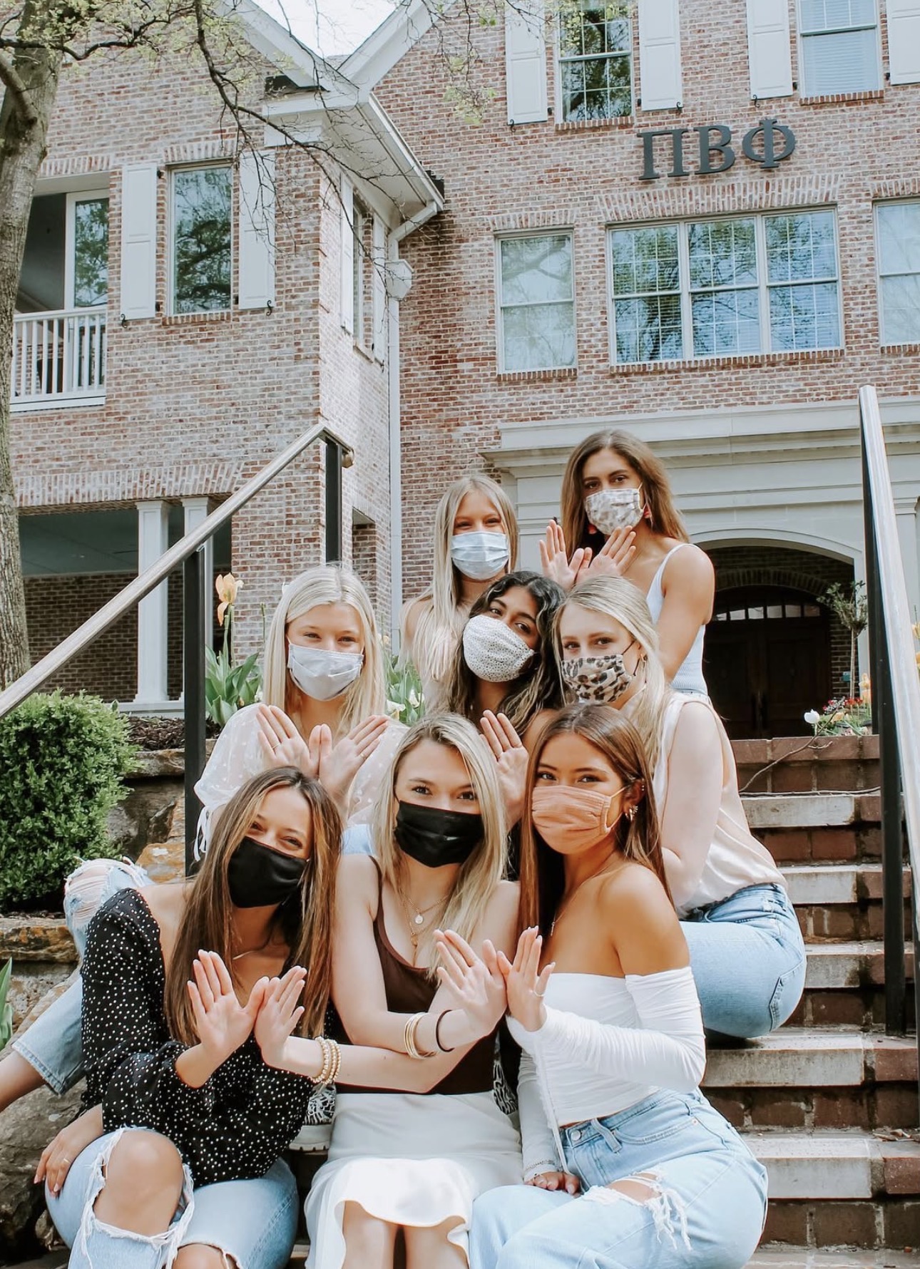 Several members sitting on an outdoor staircase in front of the chapter house wearing masks