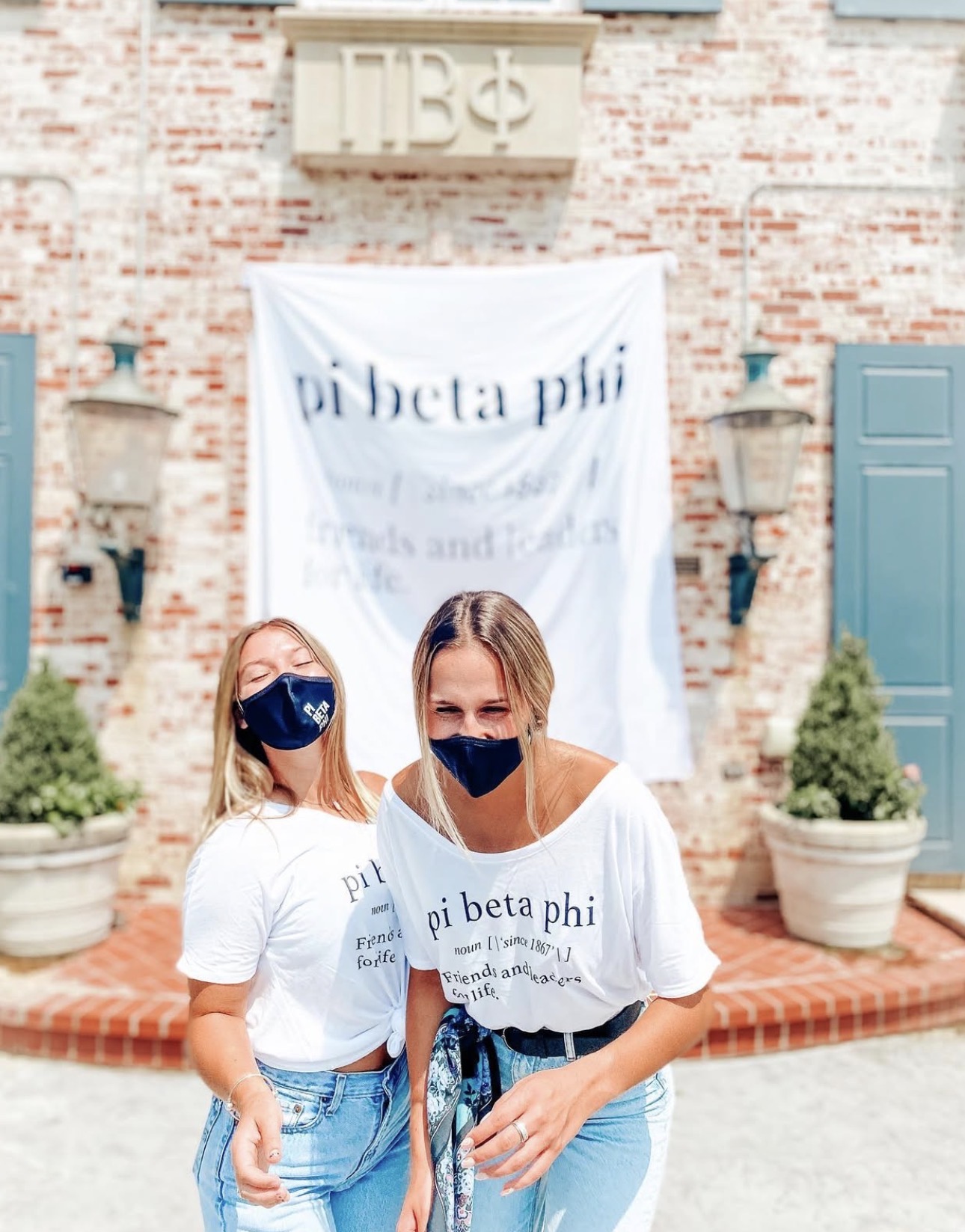 Two members wearing face masks standing in front of the chapter house with a banner that says Pi Beta Phi