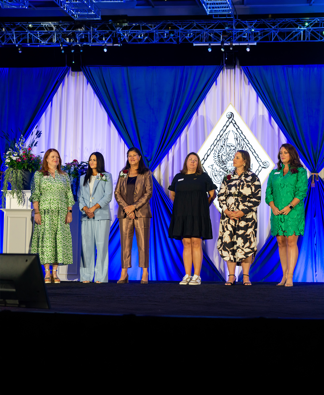 Six member standing on a stage with the crest behind them