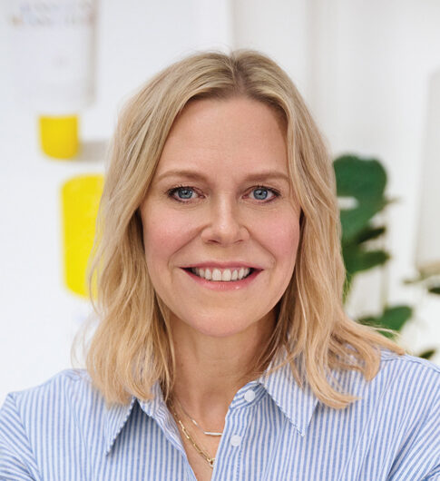 Professional headshot of Holly Thaggard wearing a blue and white striped collard shirt in front of a white background