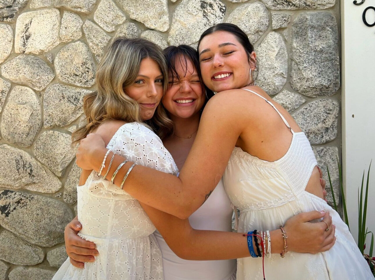 Three individuals hugging in front of a stone wall