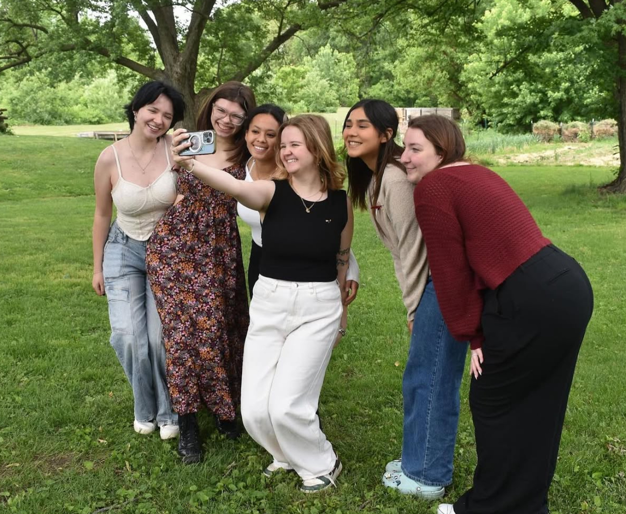 Six individuals standing in a grassy field taking a selfie