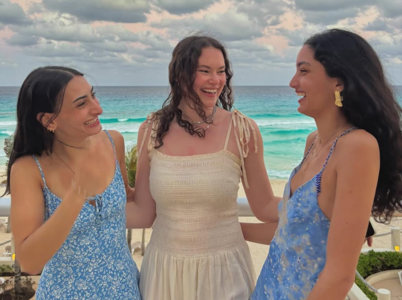 Three individuals standing on a balcony in front of the beach