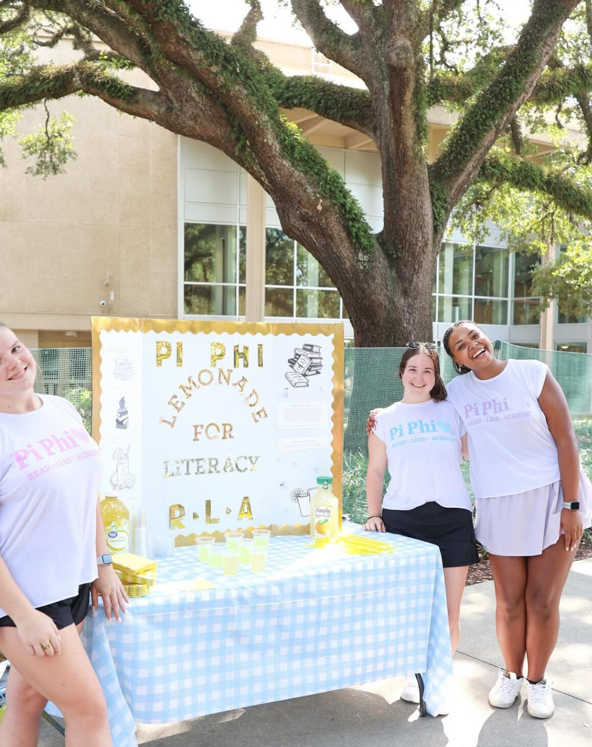 Two individuals standing next to a sign that says Pi Phi Lemonade for Literacy