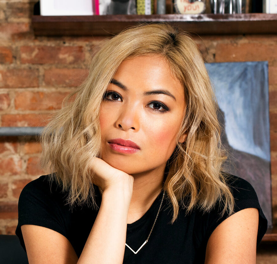 Professional headshot of Jia Tolentino resting her chin on her hand wearing a black shirt sitting in front of a brick wall