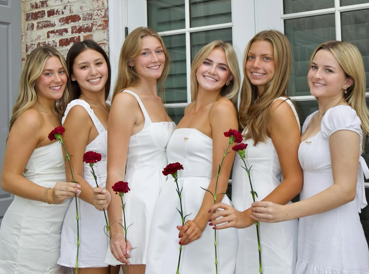 Six members wearing white and holding wine carnations