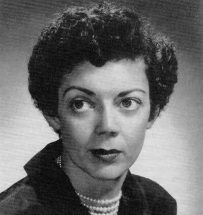 Black and white headshot of Kathryn Lyle Stephenson wearing a dark collared shirt and pearls in front of a grey background