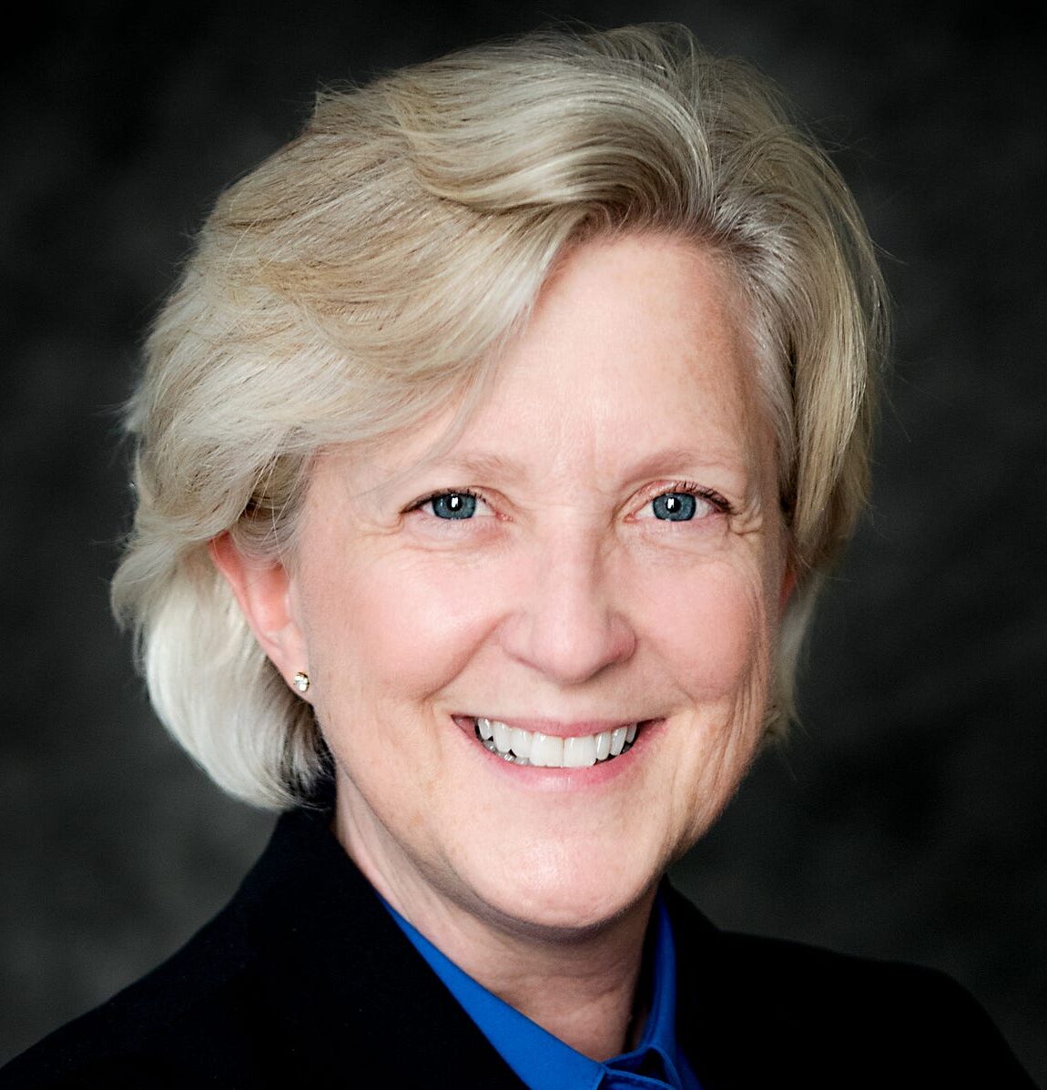 Professional headshot of Kyle Zimmer wearing a black blazer in front of a black background