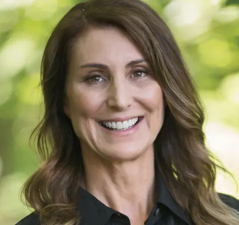 Professional headshot of Lara Merriken wearing a black collared shirt outdoors in front of trees