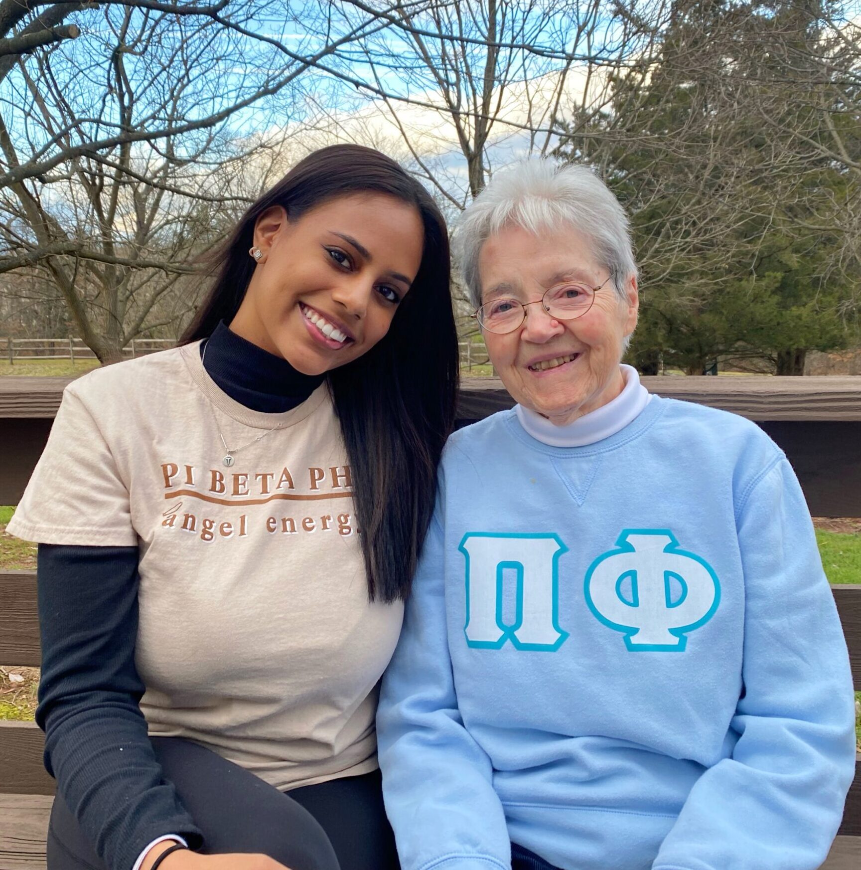An older member and younger member sitting on a bench wearing Pi Phi apparel