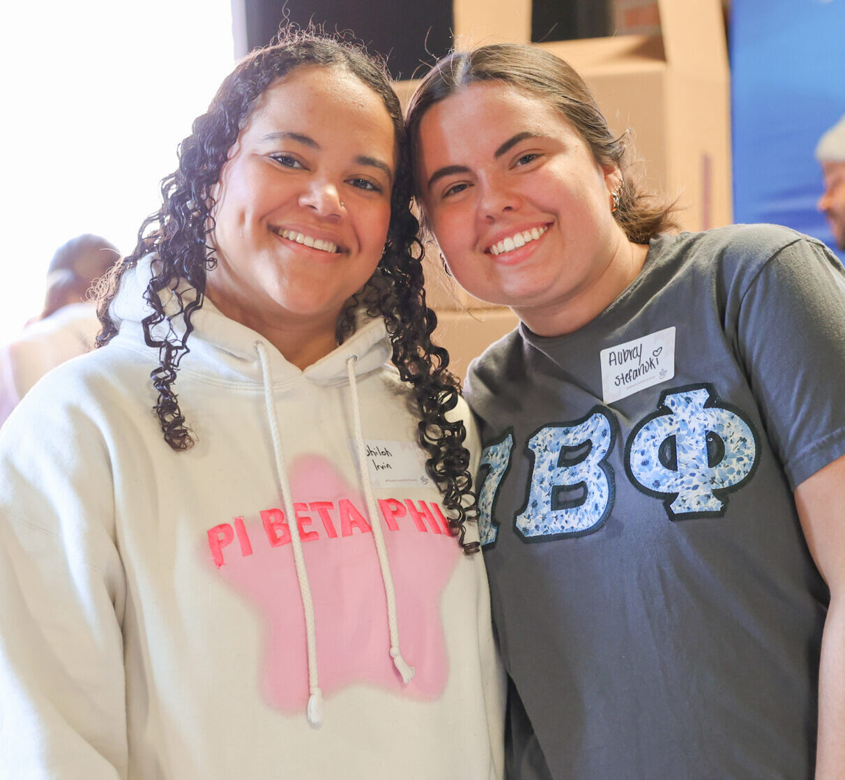 Two members standing in front of stacks of children's books wearing Pi Phi apparel