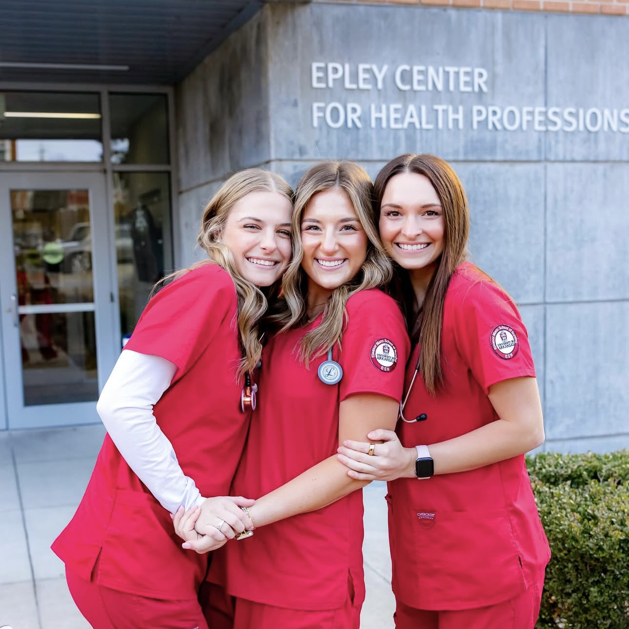 Three members wearing red scrubs in front of the Epley Center for Health Professionals