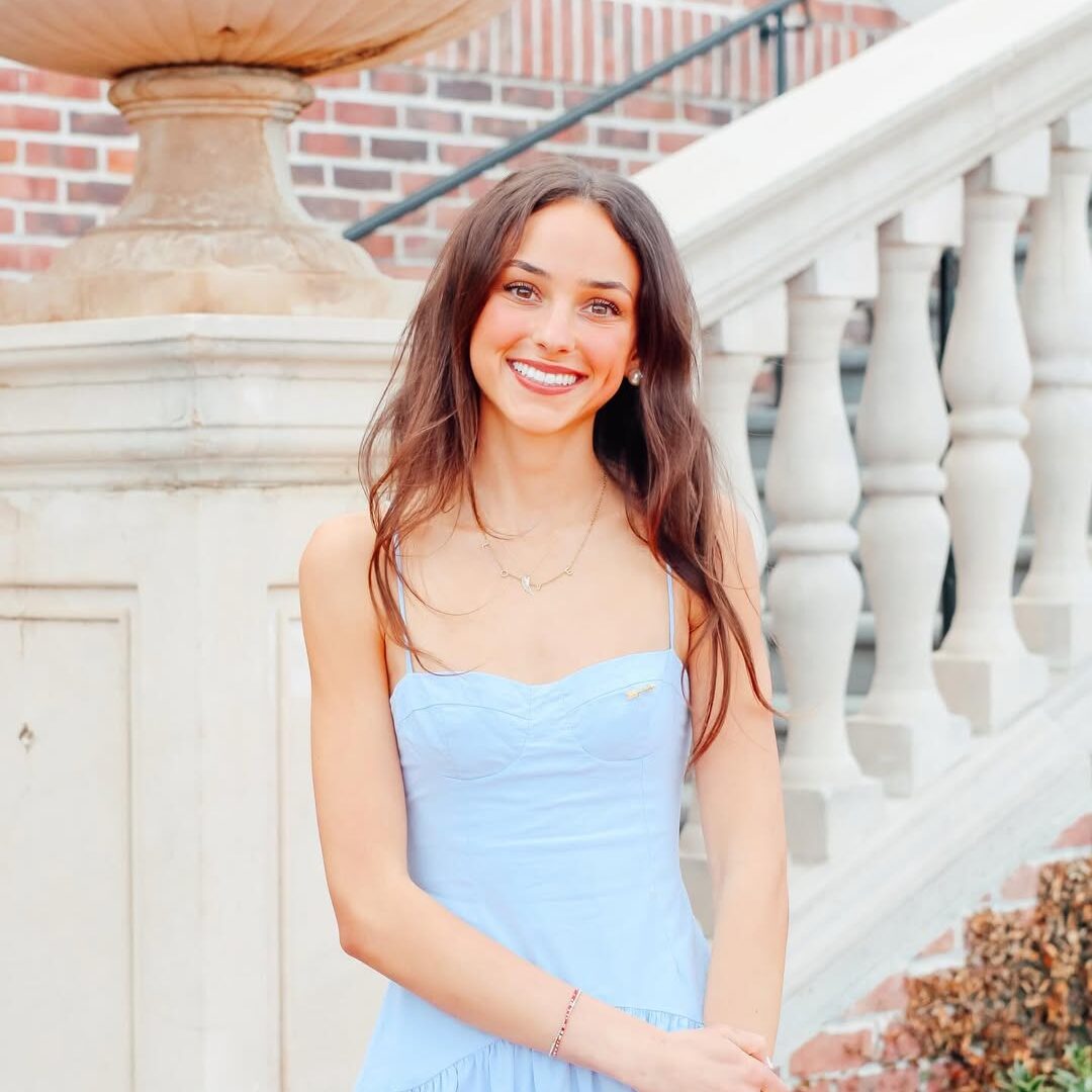 Professional headshot of Bella Walker wearing a silver blue dress and standing in front of an outdoor staircase