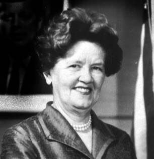 Historical black and white headshot of Leona Baumgartner wearing a dark blazer and pearl necklace in front of a dark background