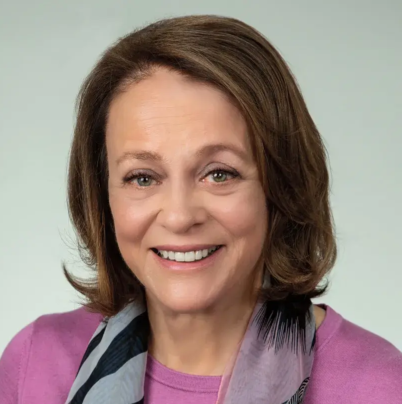 Professional headshot of Louise Bryson wearing a pink shirt with a black and white scarf in front of a grey background
