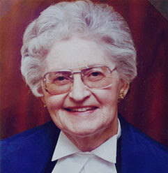 Professional headshot of Marjorie Montgomery Bowker wearing a blue shirt with a white collar and glasses in front of a maroon background