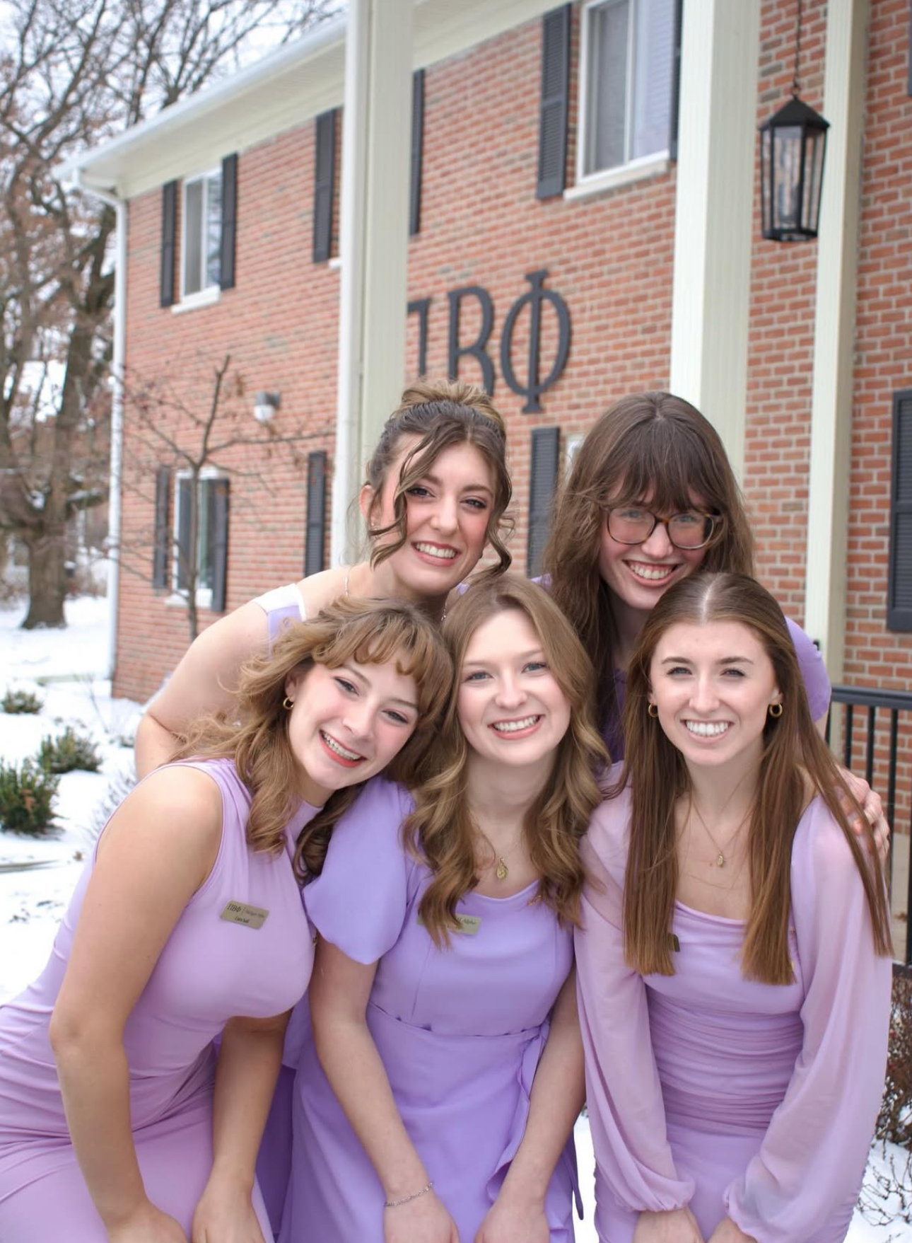 Four members wearing purple and standing in front of the chapter house