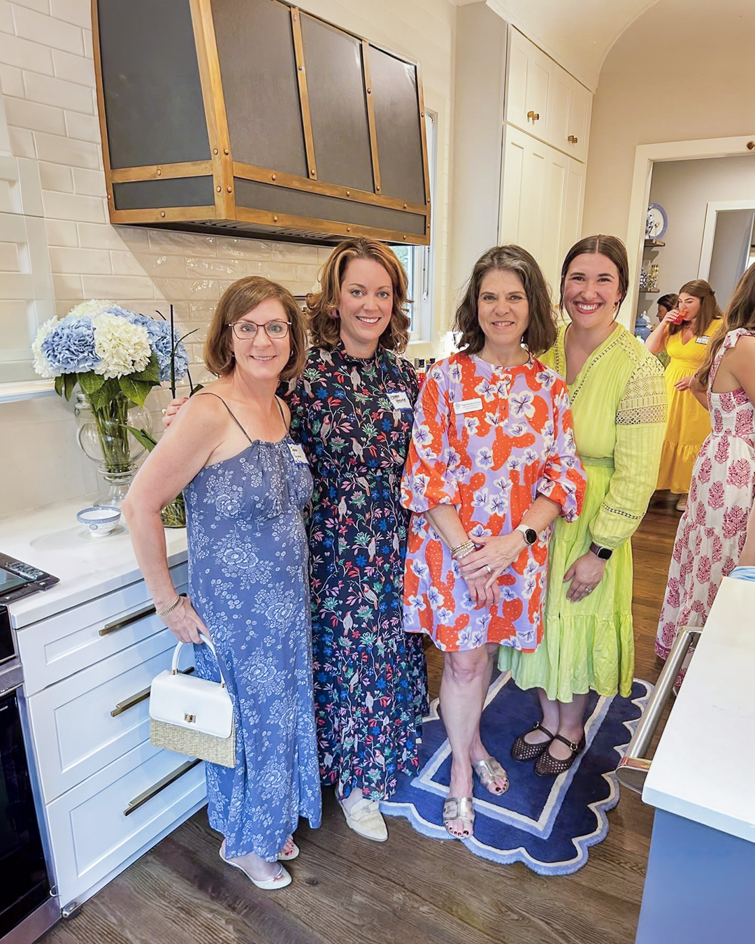 Four members standing in a kitchen wearing brightly colored dresses