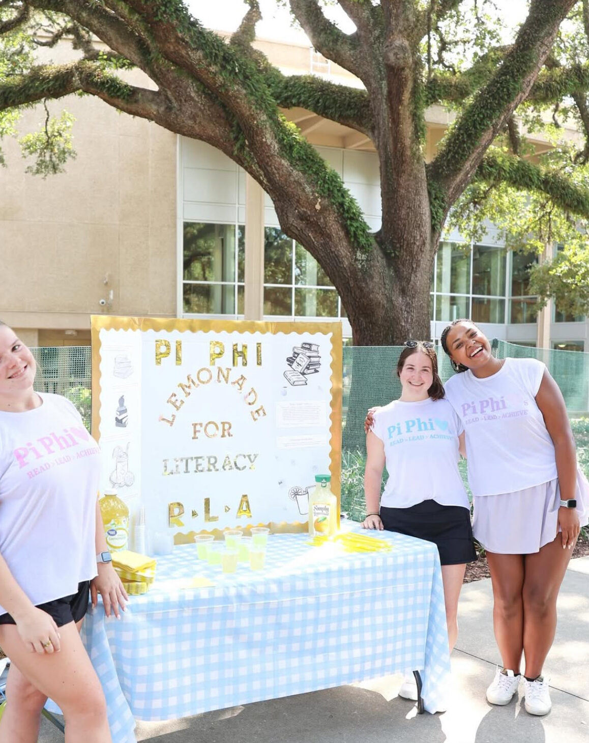 Three members standing outdoors in front of a sign that says Lemonade for Literacy