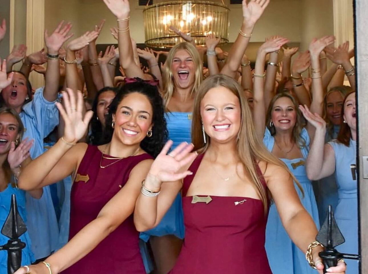 Two members wearing wine in front of several members wearing silver blue in a doorway