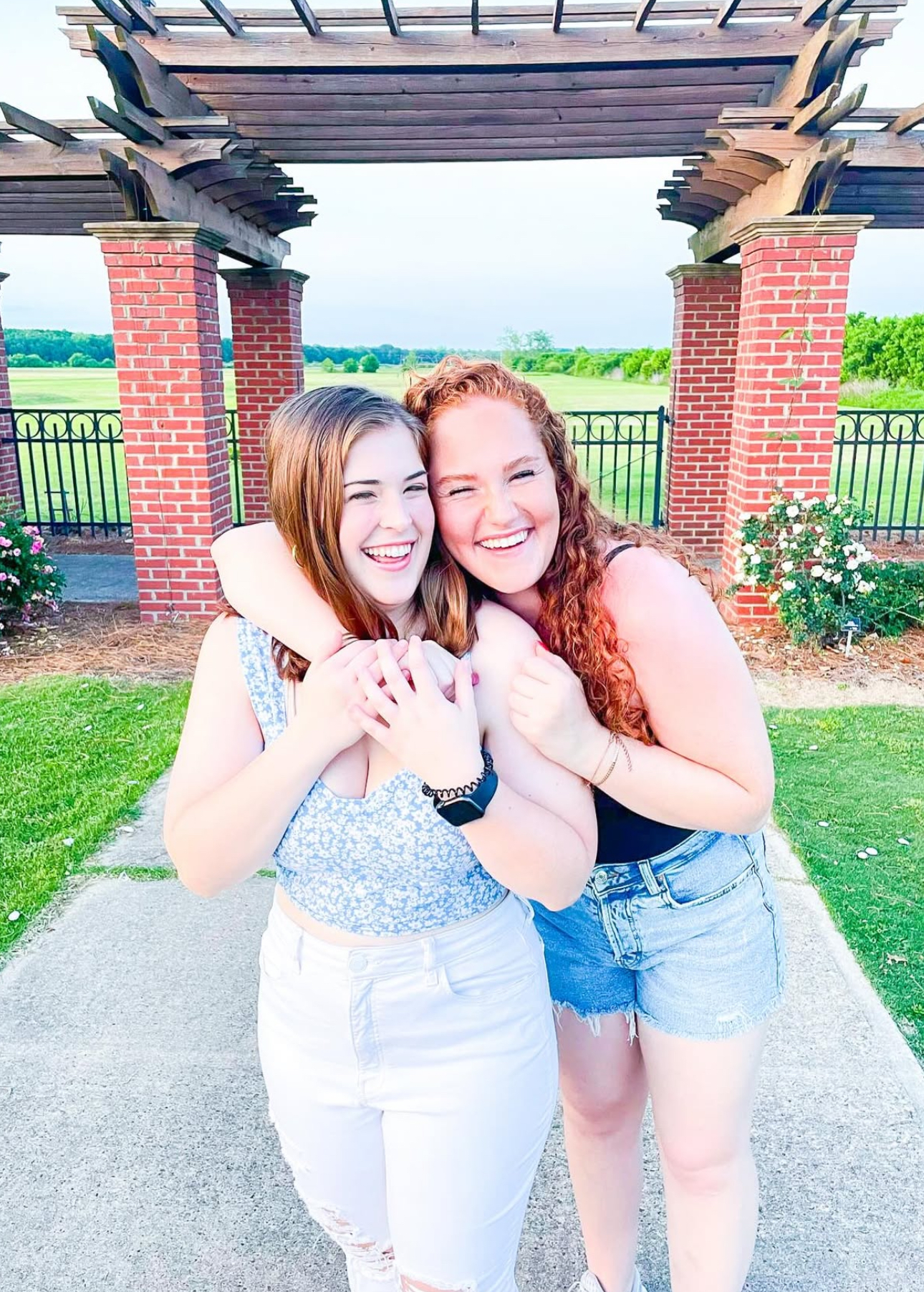 Two members hugging in front of a pergola