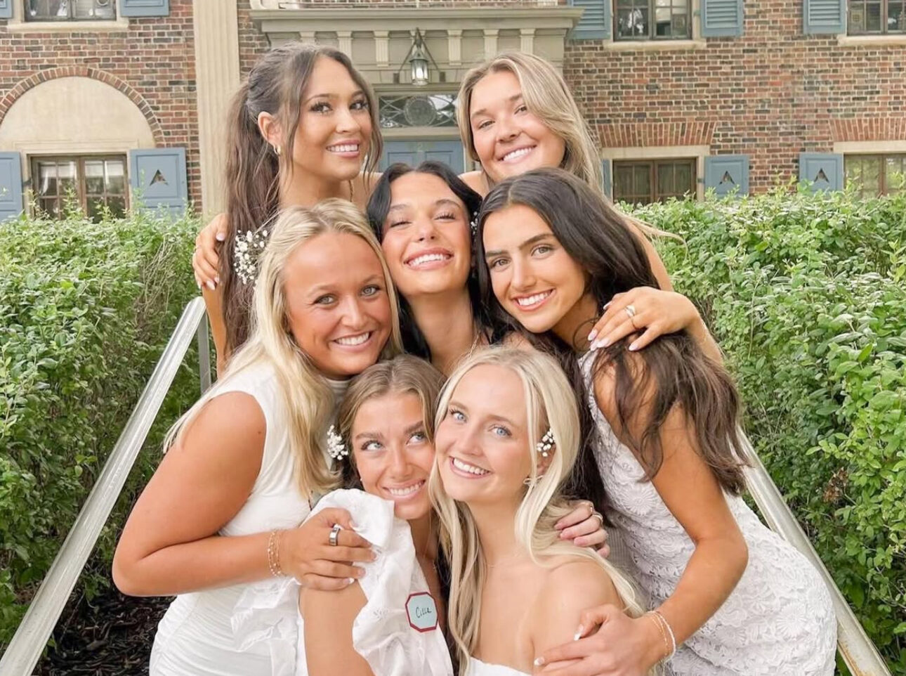 Seven members wearing white standing in front of the chapter house