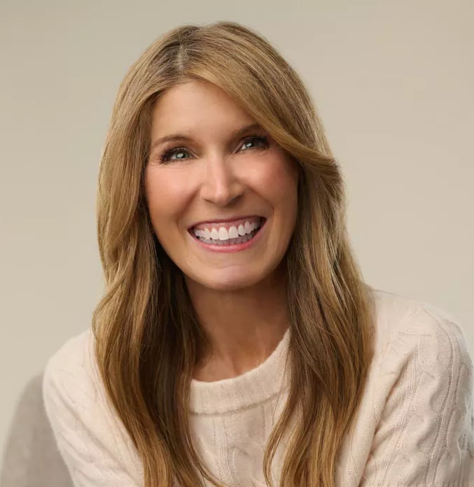 Professional headshot of Nicole Wallace wearing a white sweater in front of a cream background