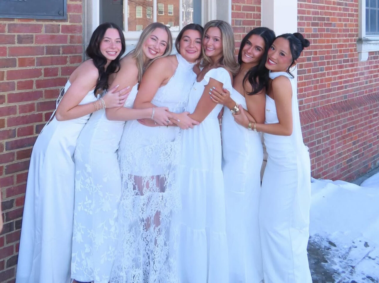 Six members wearing white dresses standing in front of the chapter house