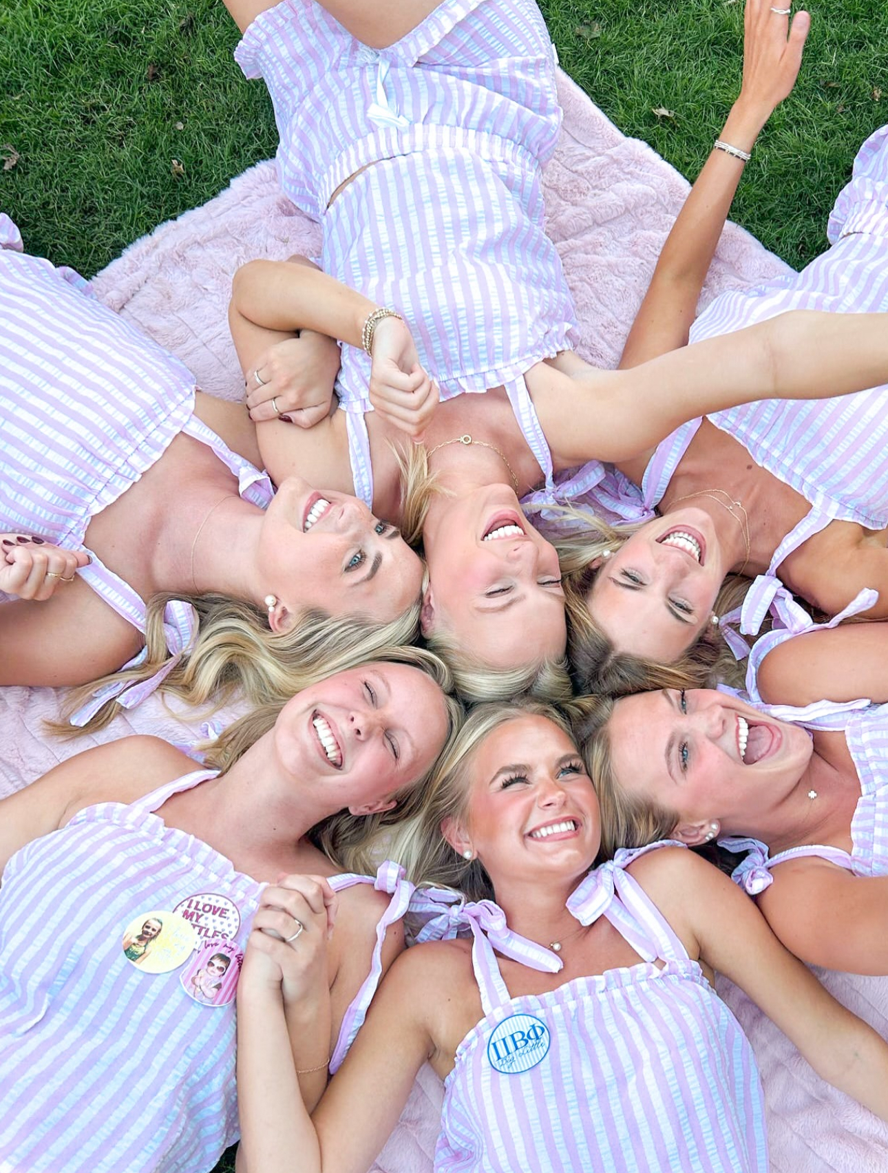 Six members lying in the grass with their heads together