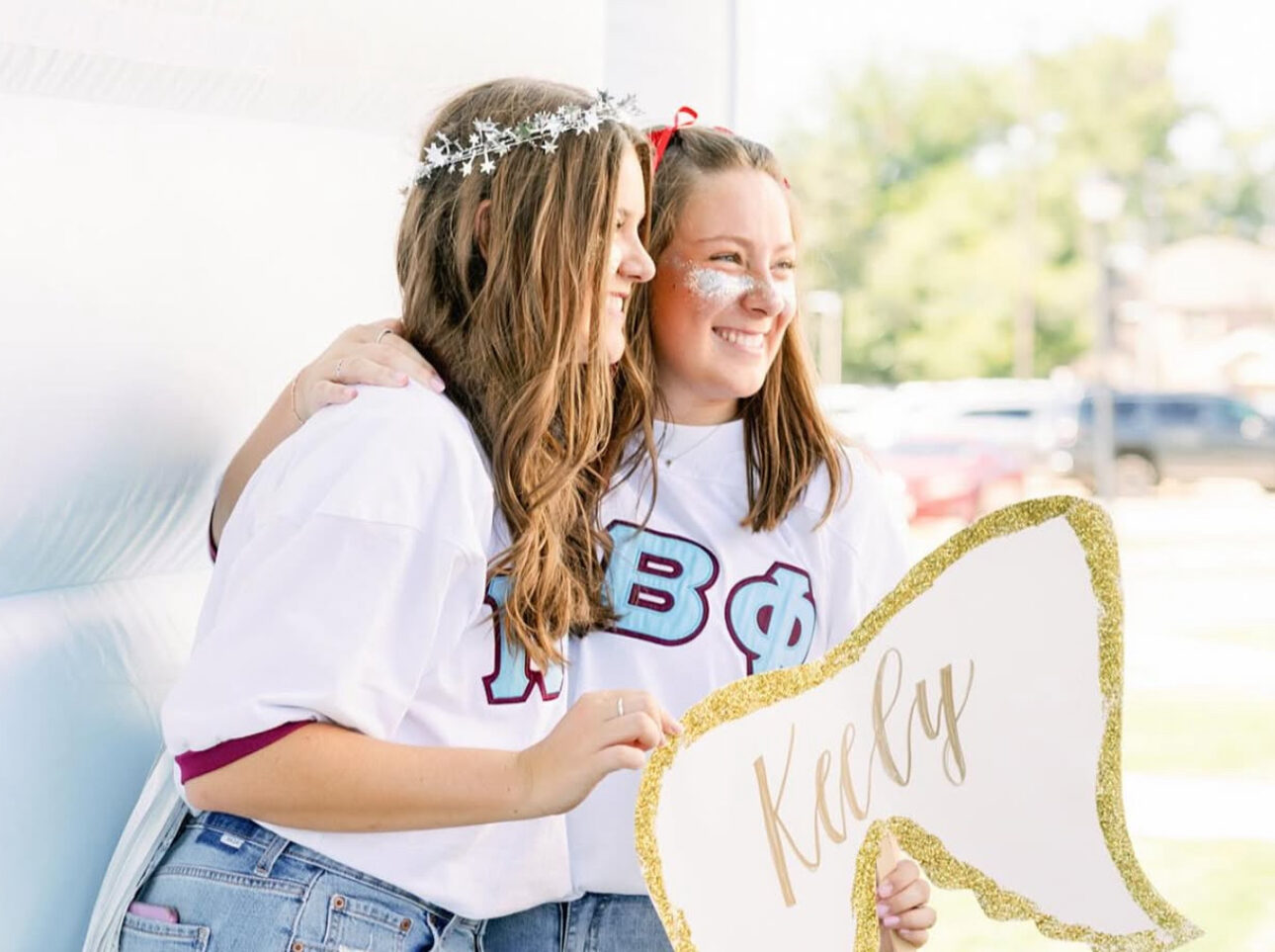 Two members wearing matching white shirts with the Pi Beta Phi Greek letters holding an angel wing sign