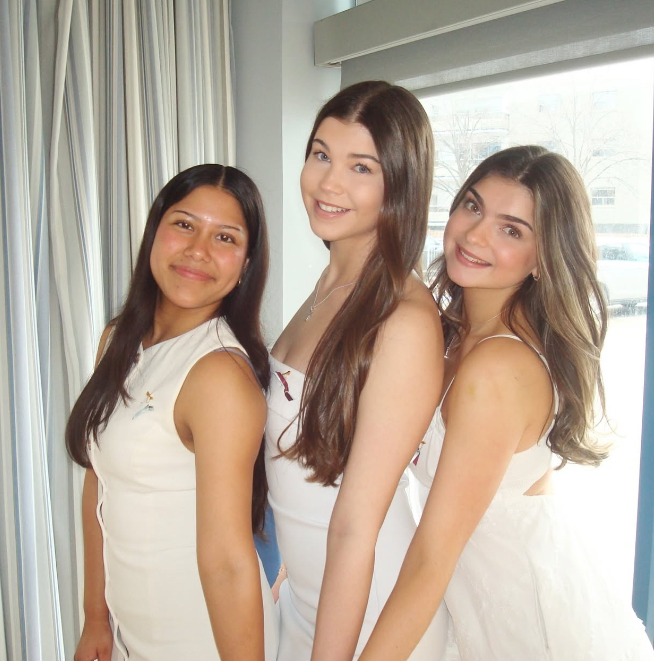 Three members wearing white and standing in front of a window