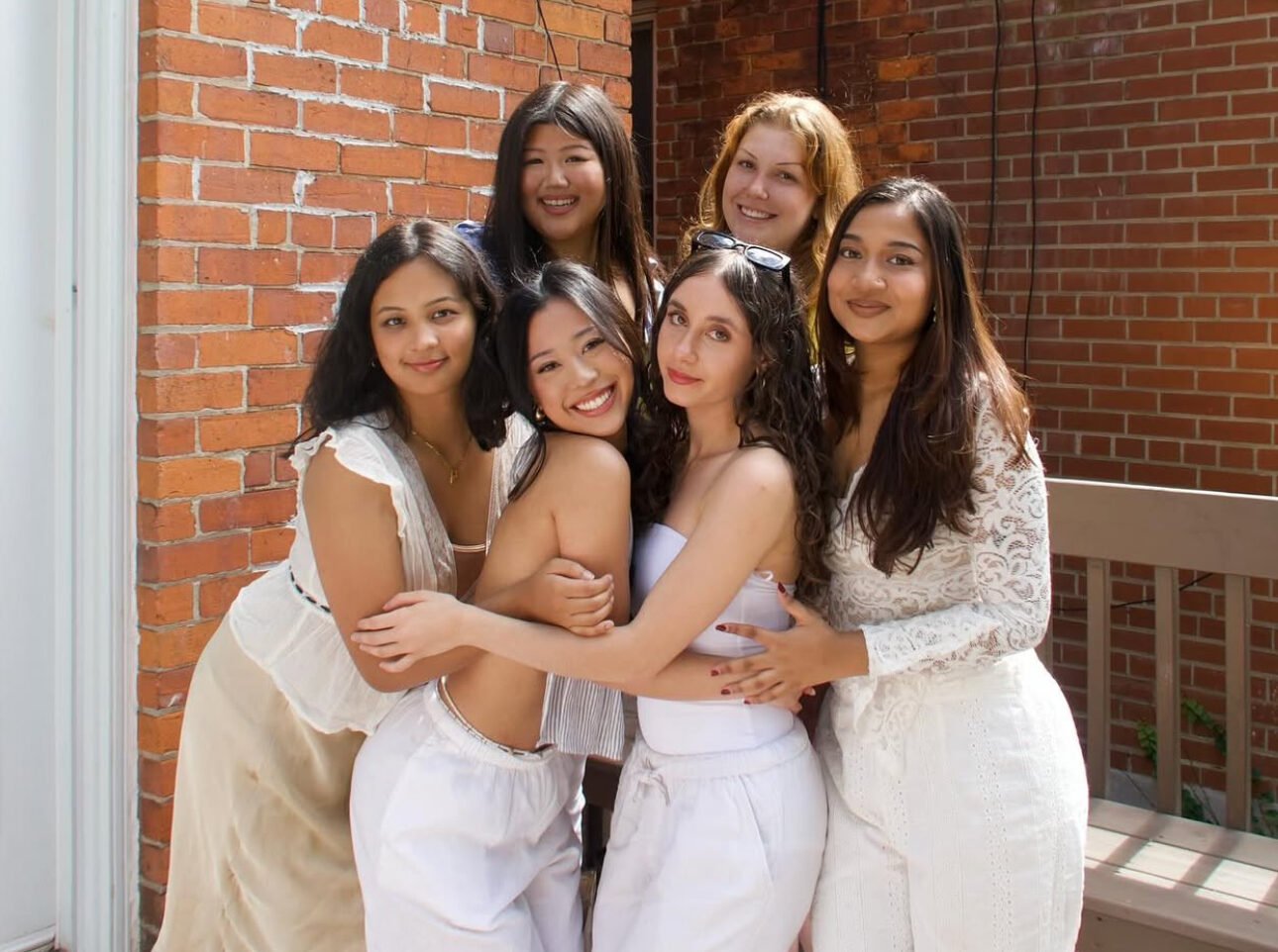 Six members wearing white hugging in front of a brick building