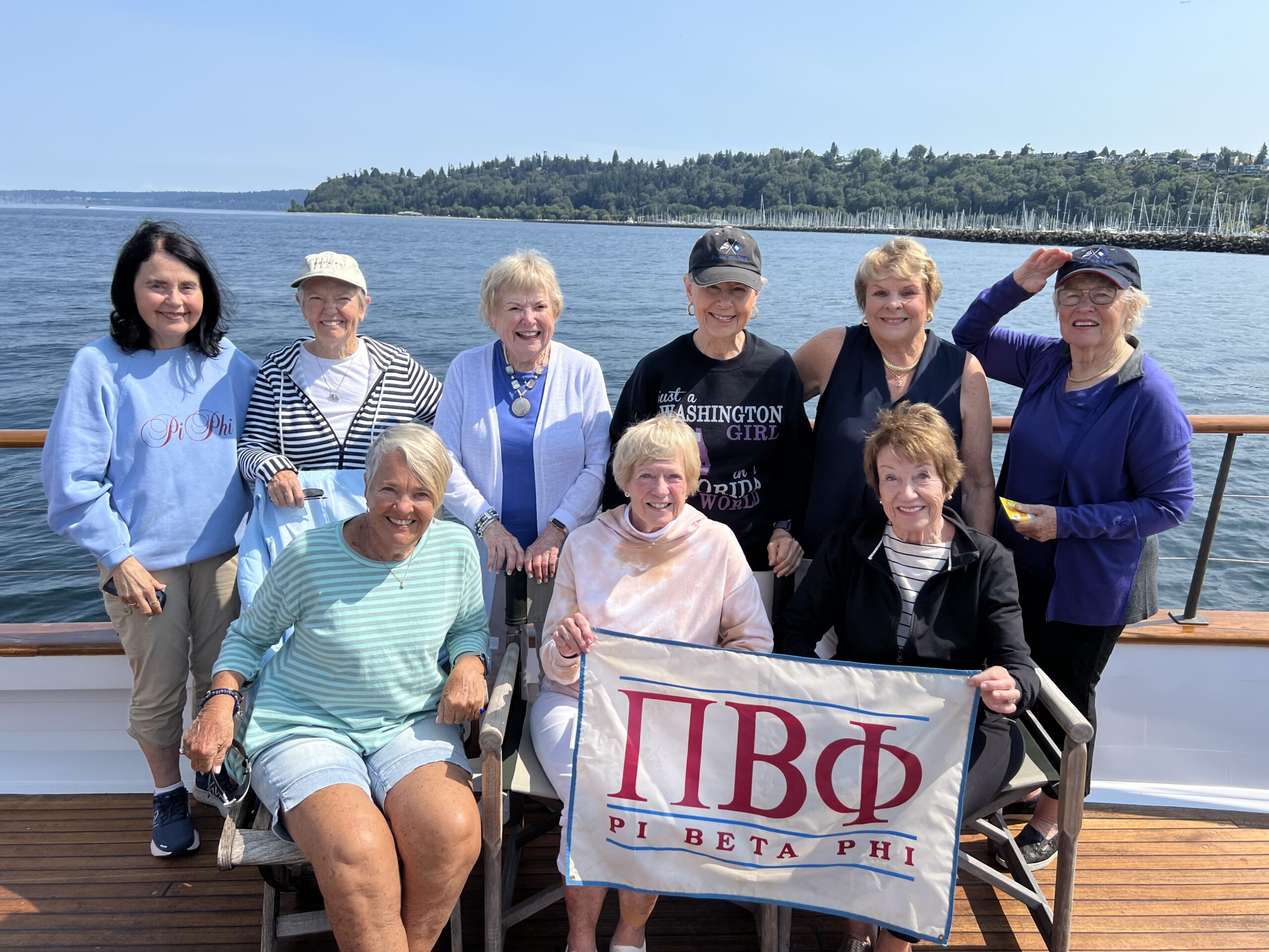 Nine individuals sitting on a cruise deck holding a Pi Phi flag