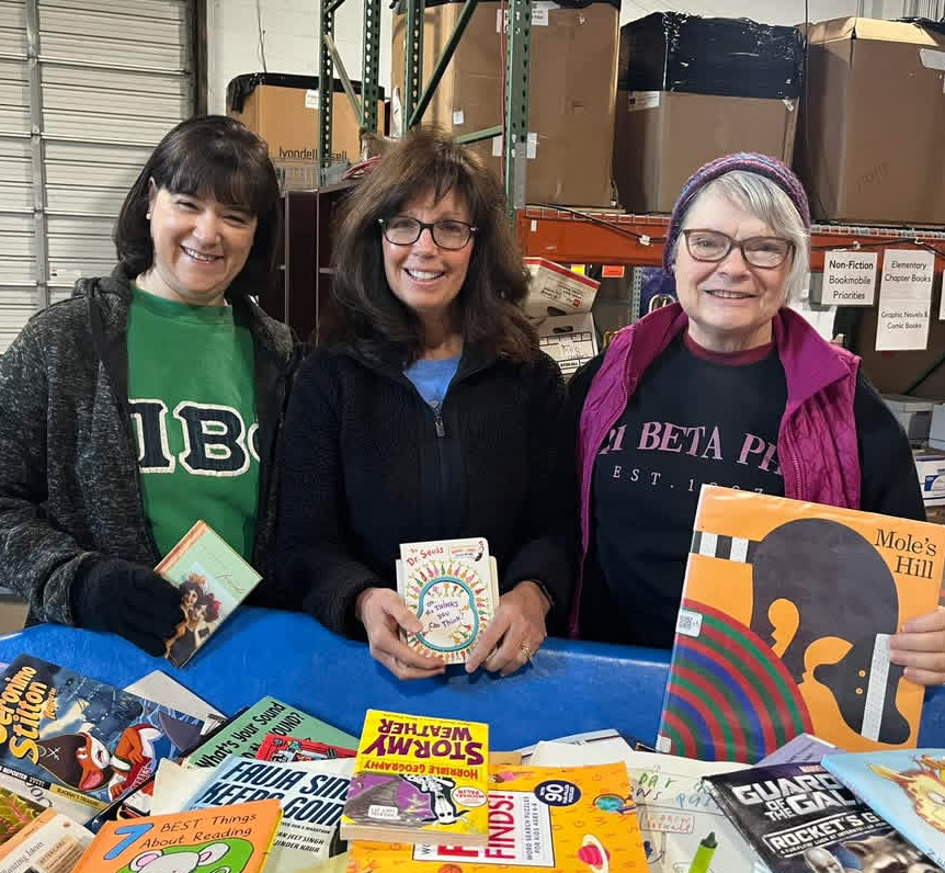 Three members standing in a warehouse holding children's books