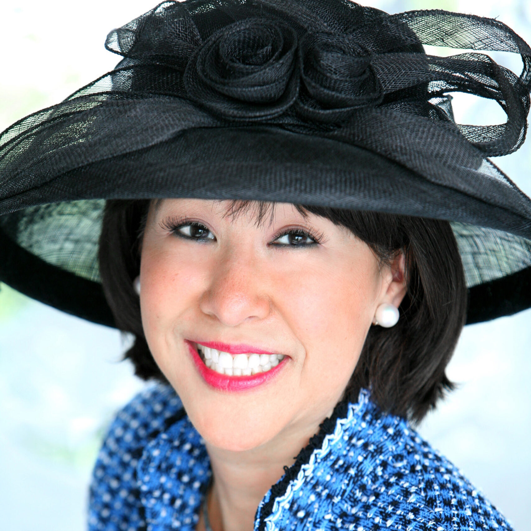 Professional headshot of Maja Berge wearing a blue patterned jacket and a black fascinator