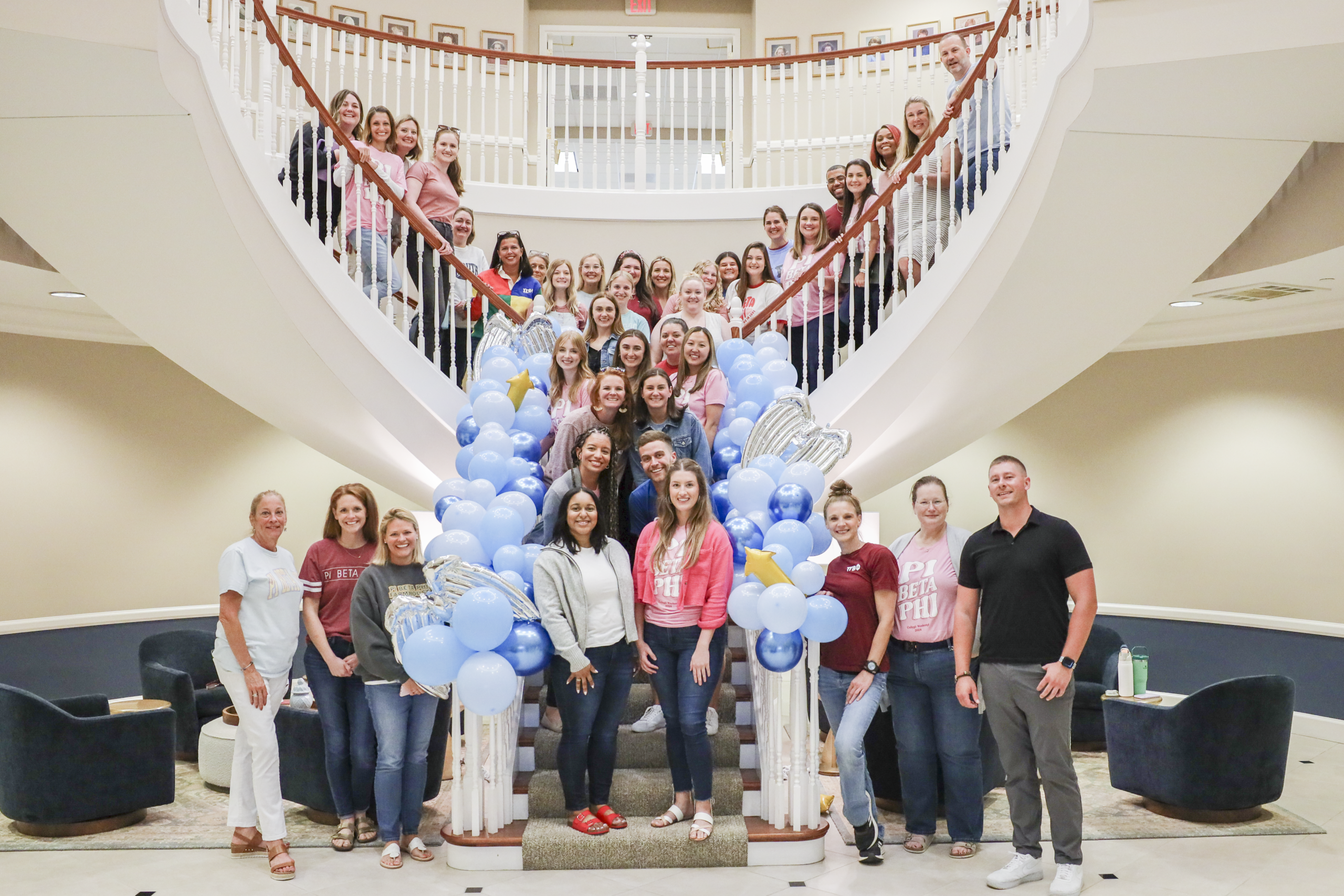 Several Pi Beta Phi Headquarters staff members standing indoors on a grand staircase with blue balloons on the railings