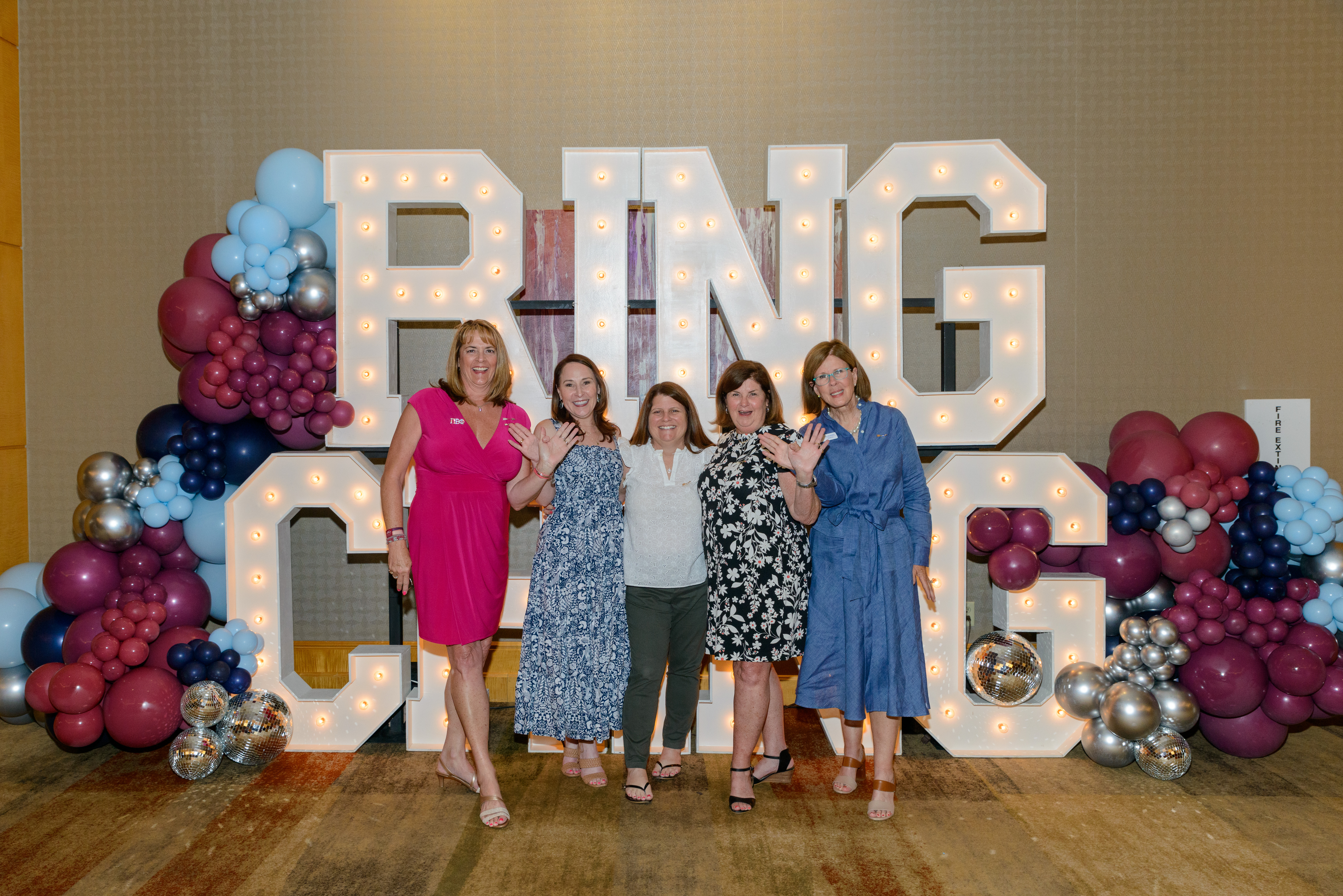 Five members standing in front of large marquee letters that say Ring Ching with wine and silver blue balloons