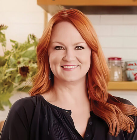 Professional headshot of Ree Drummond wearing a black shirt posing in a kitchen