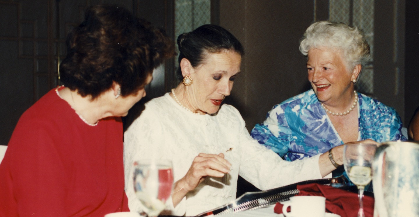 An older photo with three individuals sitting at a table and laughing