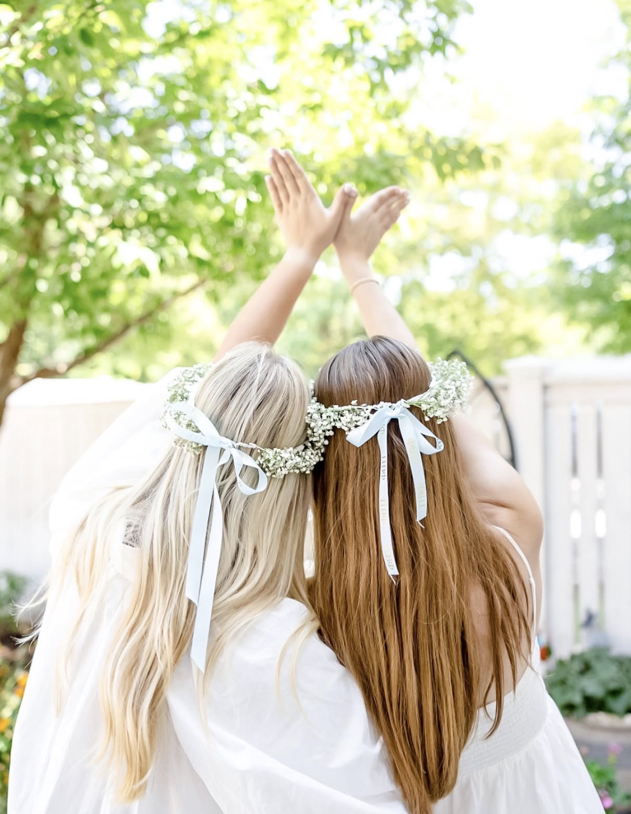 Two individuals with their back toward the camera and heads leaning together making angel wings with their hands
