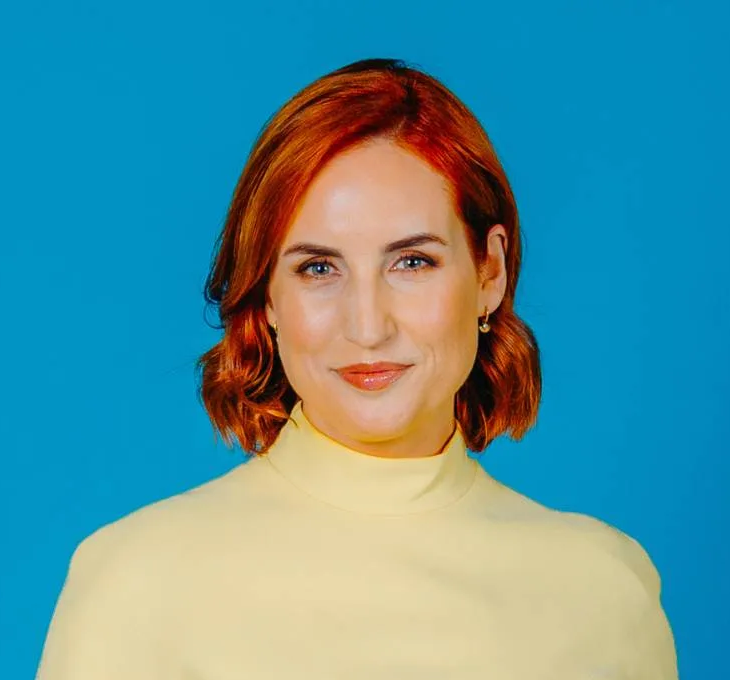 Professional headshot of Samantha Hayes wearing a yellow turtle neck in front of a blue background