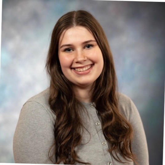 Professional headshot of Emma Spinelli wearing a gray sweater
