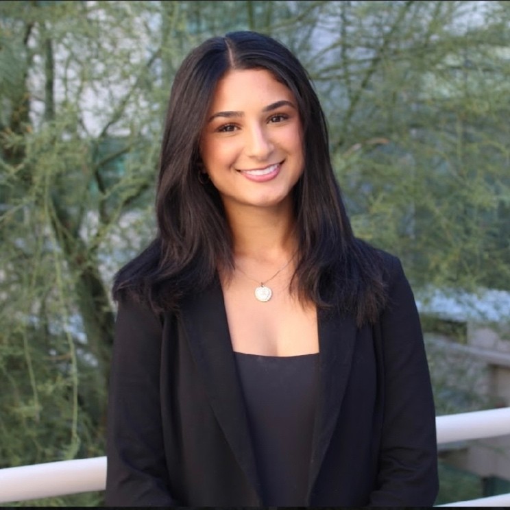 Professional headshot of Mahdiya Aziz wearing a black jacket and blouse in front of a tree