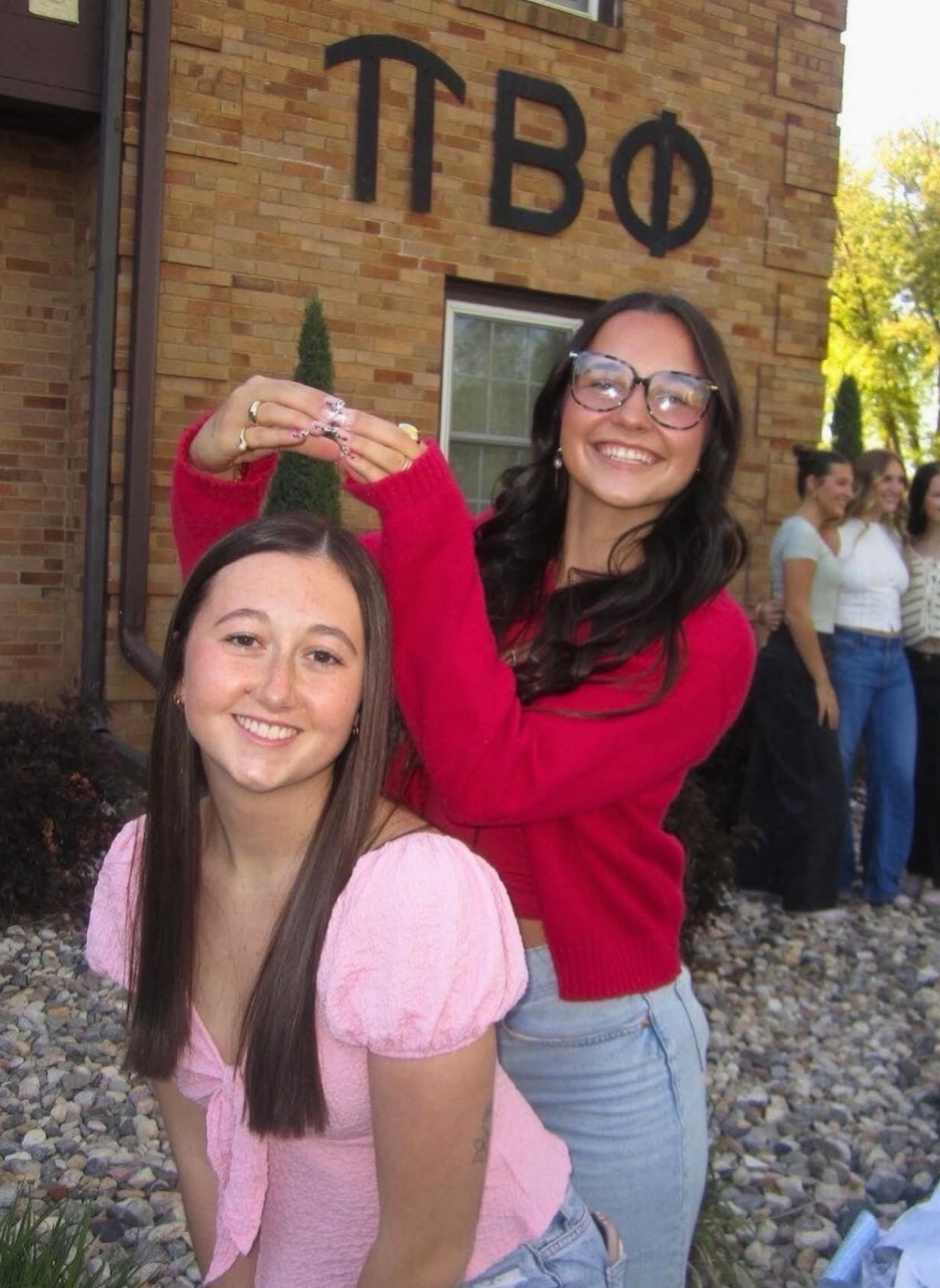 Two members standing in front of the chapter house. One member making a halo with her hands above the others' head