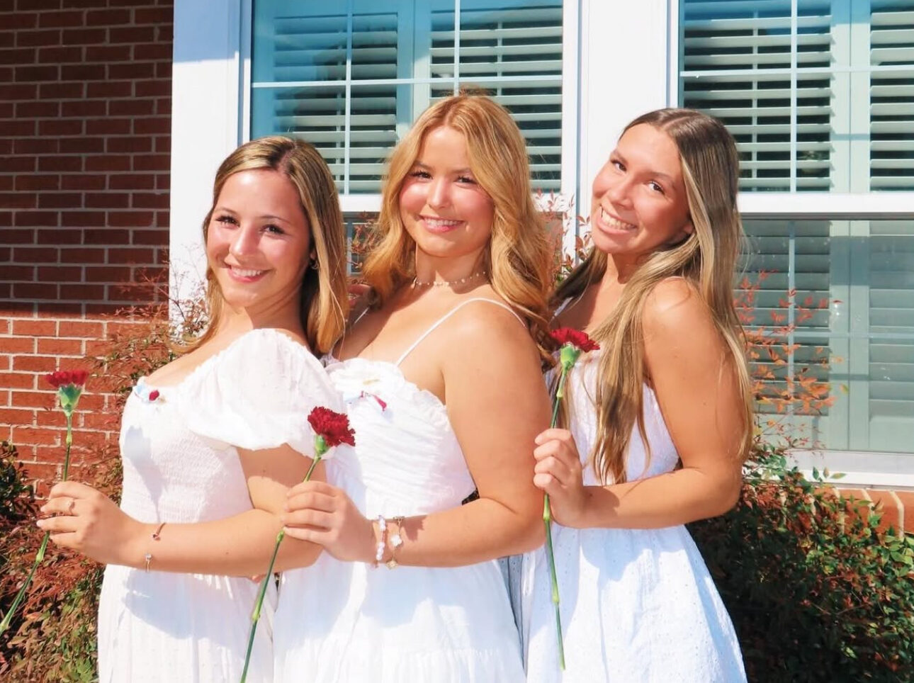 Three members wearing white standing in front of the chapter house