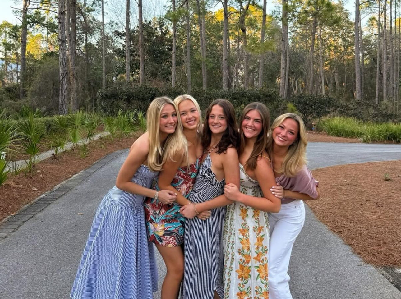 Five members standing on a road in front of trees